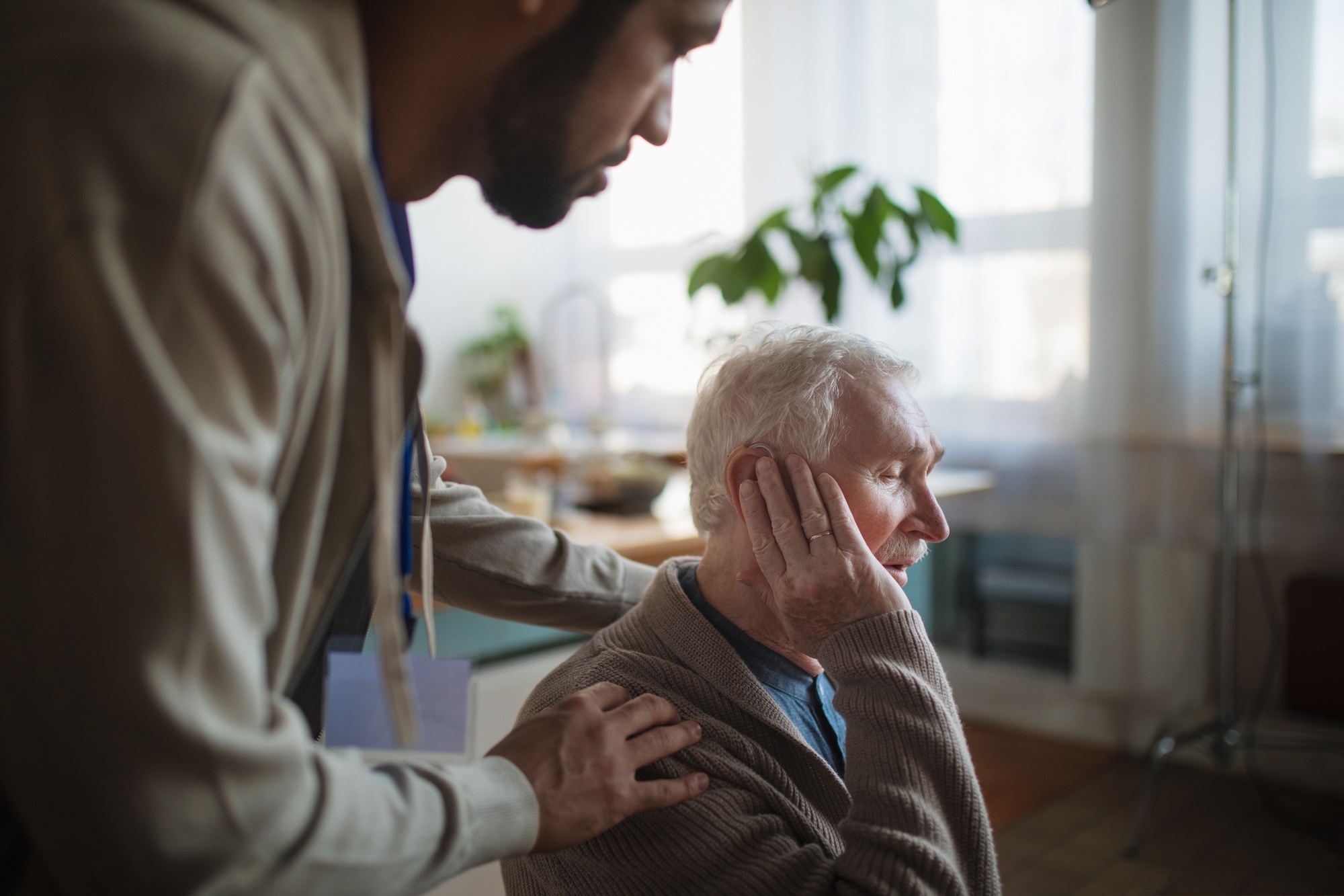 Caregiver helping seniot man to insert hearing aid in his ear