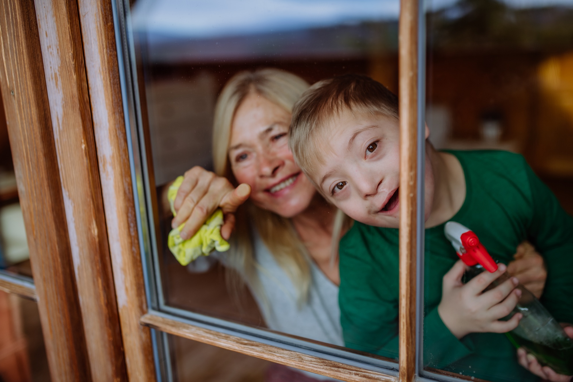 Boy with Down syndrome with his grandmother cleaning window at home