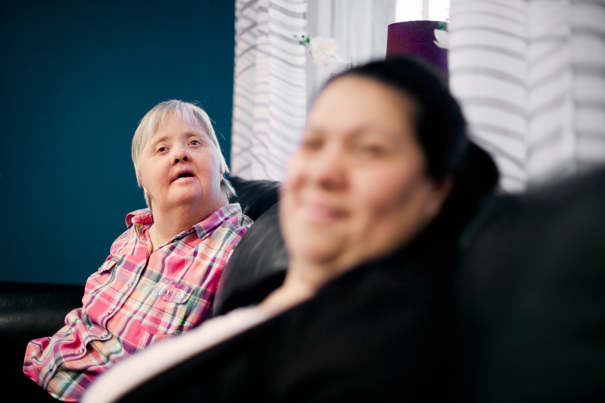 Mentally challenged woman sitting with friend on sofa at home