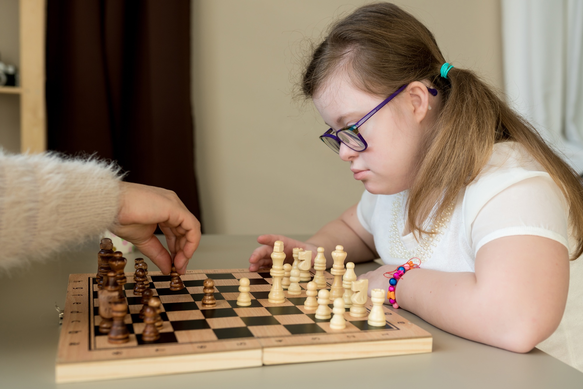 Teenager girl with Down syndrome playing chess on the game board